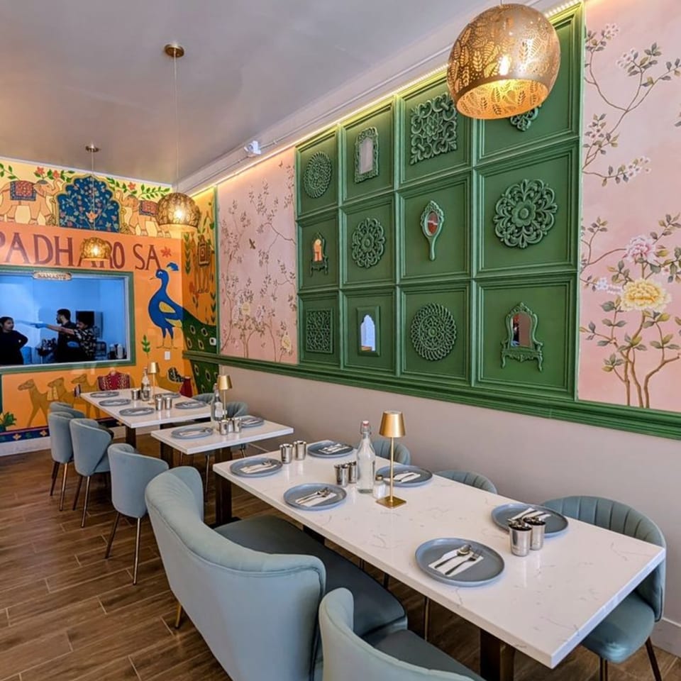 Interior of Garam Mirchi restaurant with colorful Indian-themed murals, green paneled walls, and set tables.