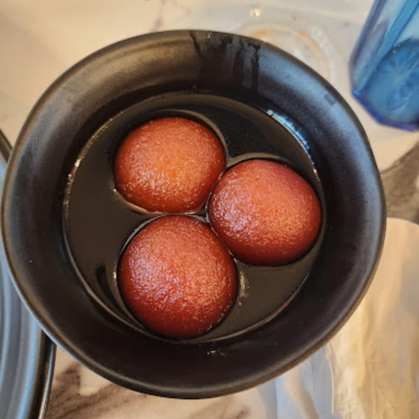 Three gulab jamuns, Indian fried dough balls soaked in syrup, in a black bowl.