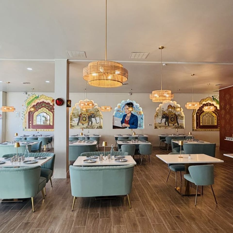 Garam Mirchi restaurant interior with light blue chairs, white tables, and Indian-themed wall art.