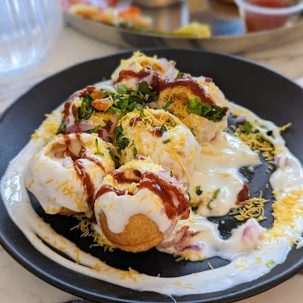 A plate of Indian dahi puri, topped with yogurt, chutneys, chopped onions, and cilantro.