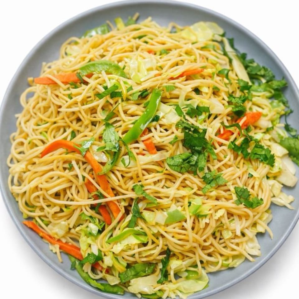 A plate of Indo-Chinese noodles with carrots, cabbage, green peppers, and cilantro.