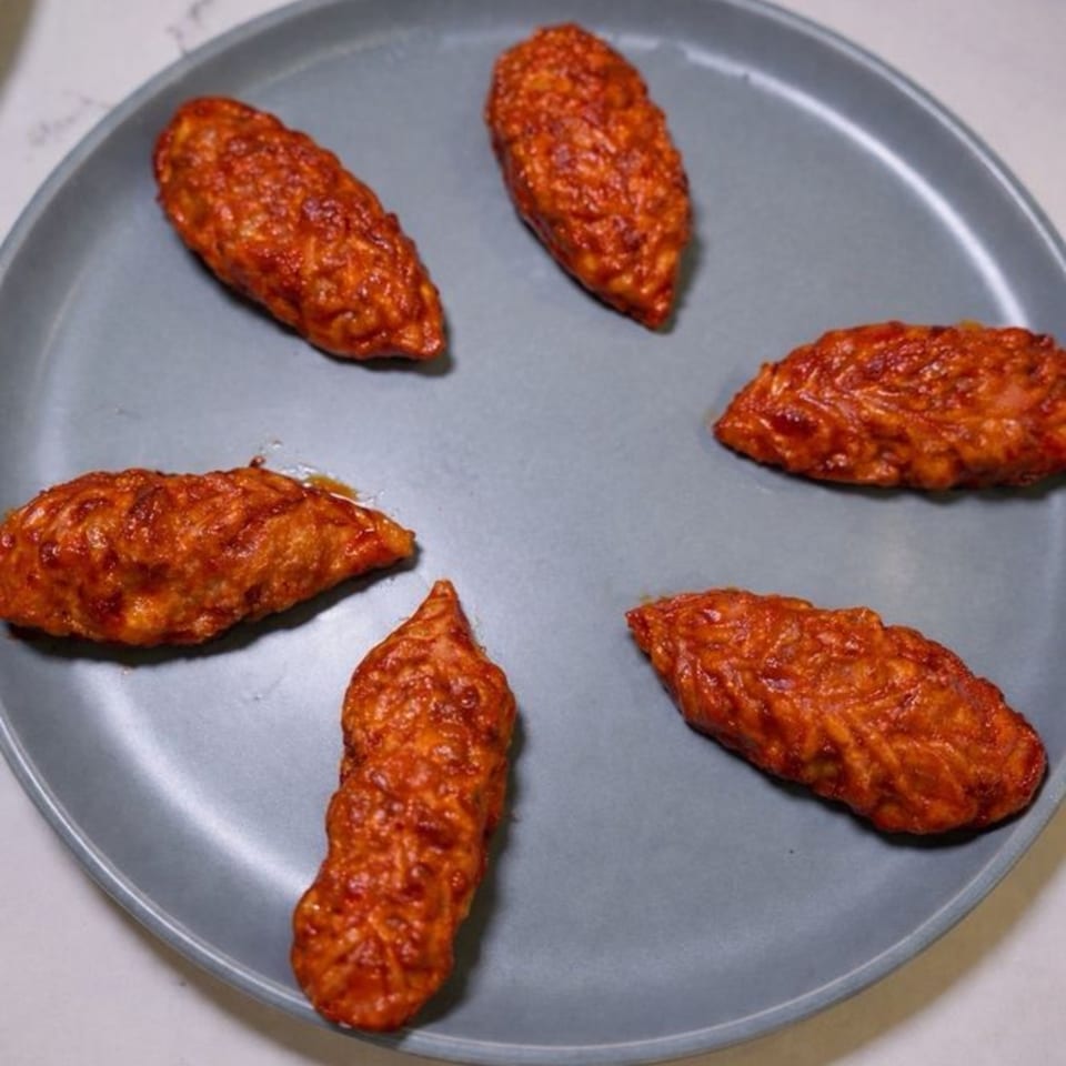 Six vibrant orange-red Indian dumplings, possibly momos or gujiyas, arranged on a gray plate.