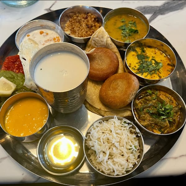 A Garam Mirchi thali with various Indian dishes, including curries, rice, bread, and a drink.