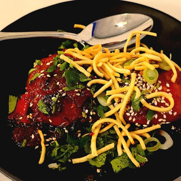 Indo-Chinese dish with red sauce, sesame seeds, cilantro, green onions, and crispy noodles.