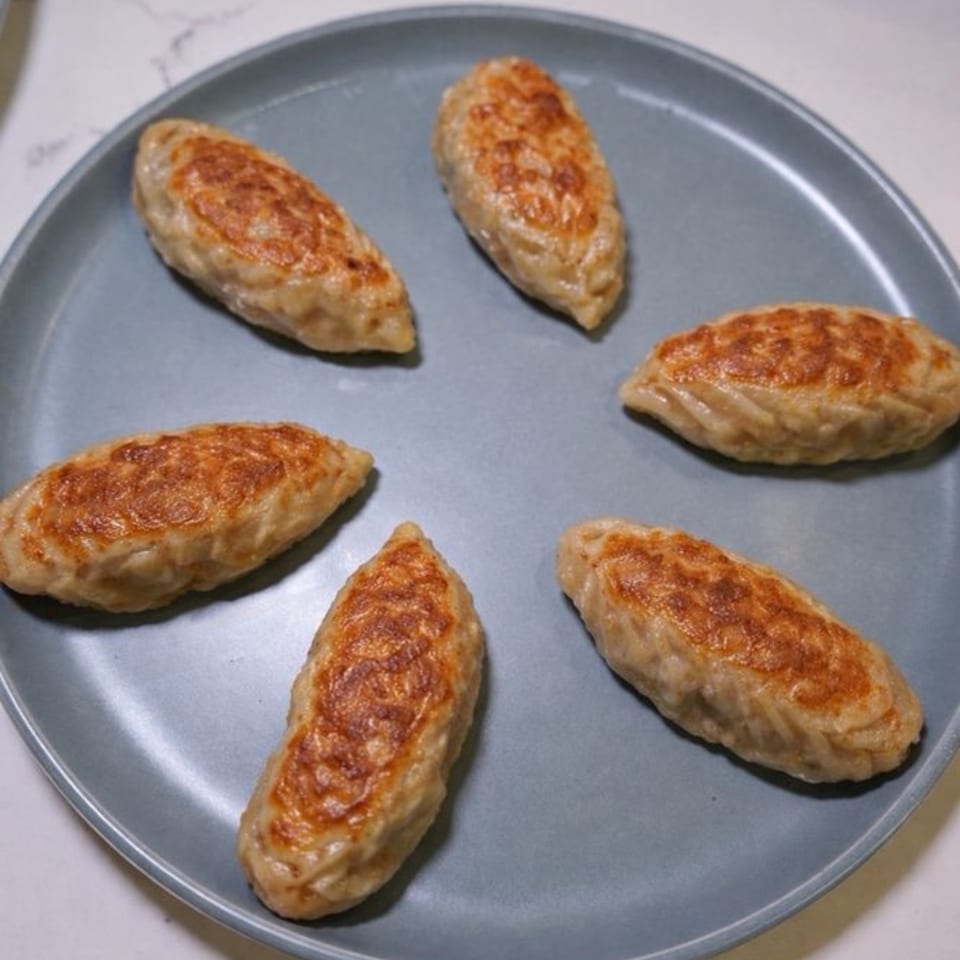 Six pan-fried dumplings with golden-brown crusts arranged in a circle on a gray plate.