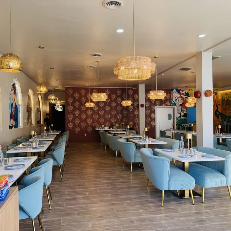 The Garam Mirchi restaurant interior features light blue chairs, white tables, and Indian-inspired decor with ornate lighting.
