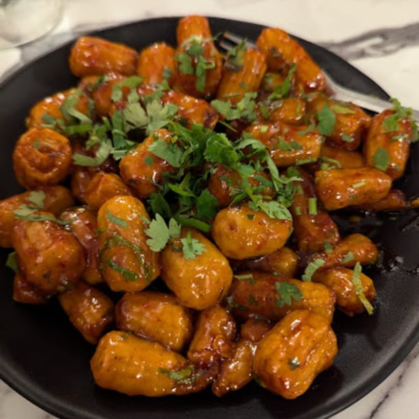 A black plate filled with golden-brown, glazed Indo-Chinese potato bites, garnished with fresh green cilantro.