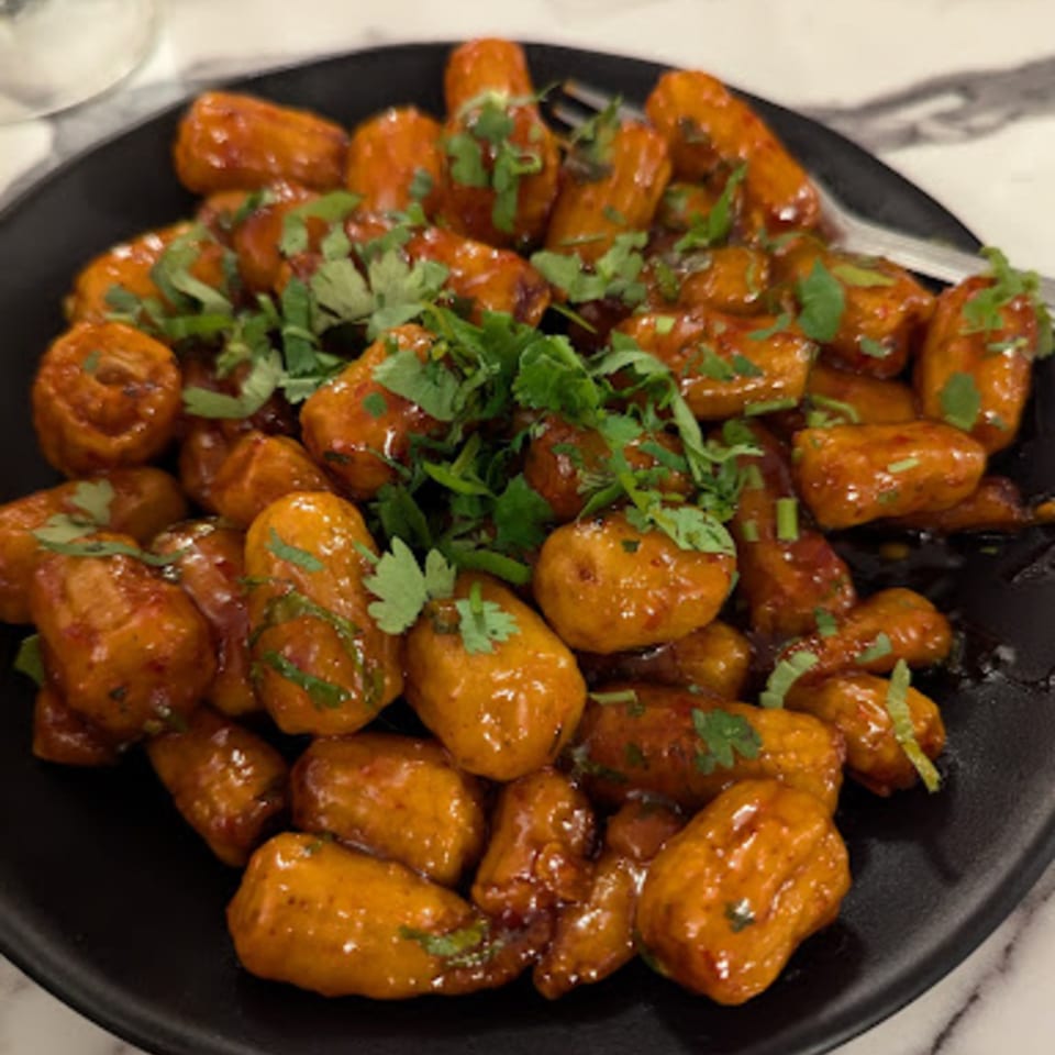 A black plate filled with golden-brown, glazed Indo-Chinese potato bites, garnished with fresh green cilantro.